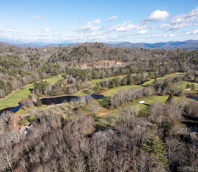 view of property location with a water and mountain view, a local golf course, and a forest