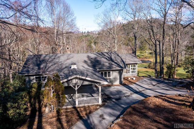view of front facade with asphalt driveway, a porch, and a wooded view