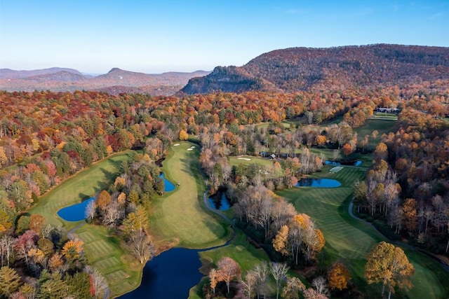 aerial view of property and surrounding area with a heavily wooded area, a golf club, and a water and mountain view