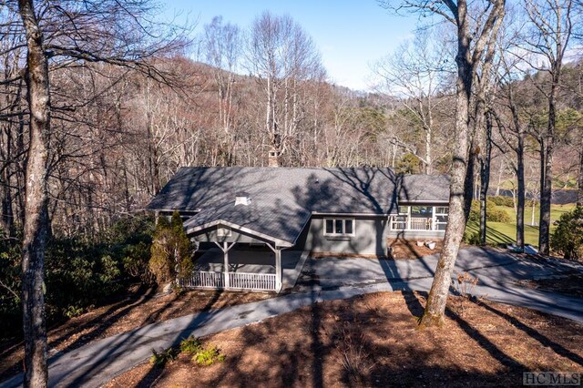 view of front facade with aphalt driveway, covered porch, a wooded view, and a chimney