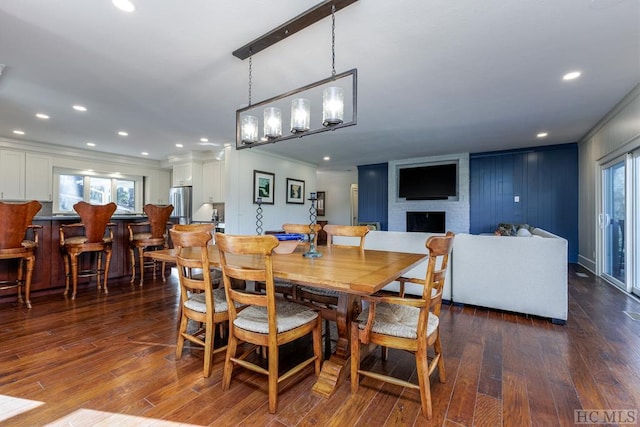 dining space featuring ornamental molding, healthy amount of natural light, dark wood-style flooring, a fireplace, and recessed lighting