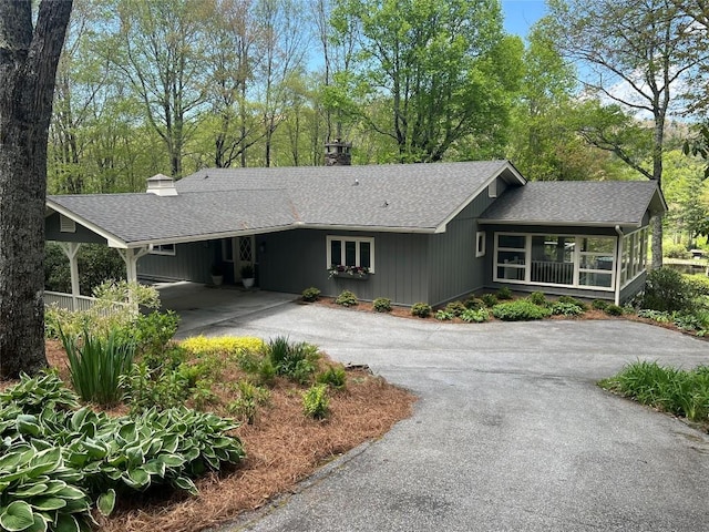 view of front of house with driveway, a chimney, roof with shingles, a carport, and a porch