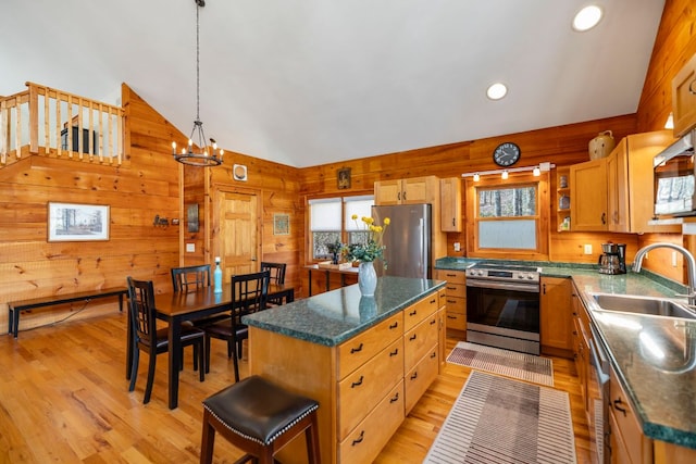 kitchen featuring stainless steel appliances, light wood-type flooring, a sink, and wood walls