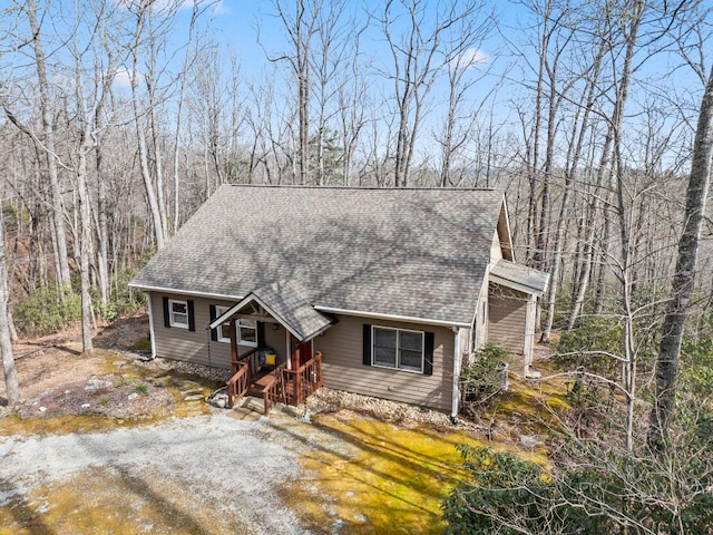 view of front of property with driveway, roof with shingles, and a wooded view