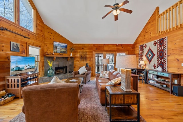 living room featuring a wealth of natural light, wood walls, a stone fireplace, and wood finished floors