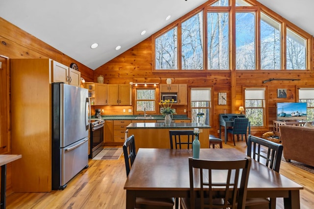 dining room featuring high vaulted ceiling, light wood-style flooring, and wooden walls