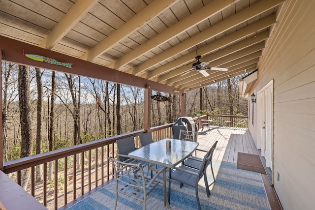 wooden terrace featuring a ceiling fan, outdoor dining area, and a wooded view