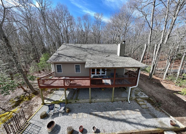 rear view of property with a shingled roof, a chimney, and a deck