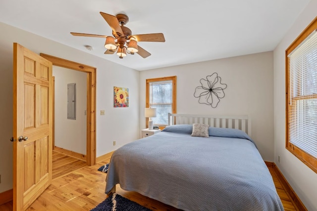 bedroom with light wood-style flooring, electric panel, baseboards, and a ceiling fan