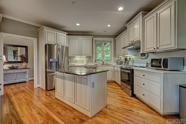 kitchen with dark stone counters, a kitchen island, stainless steel appliances, white cabinets, and ornamental molding