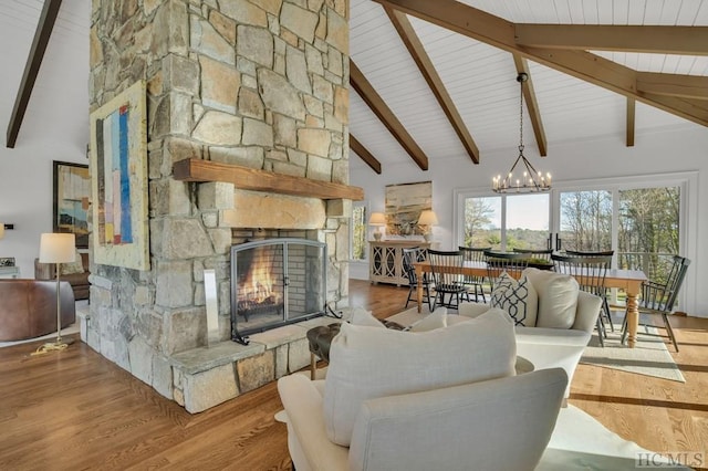 living room featuring beam ceiling, light wood-type flooring, a notable chandelier, and a stone fireplace