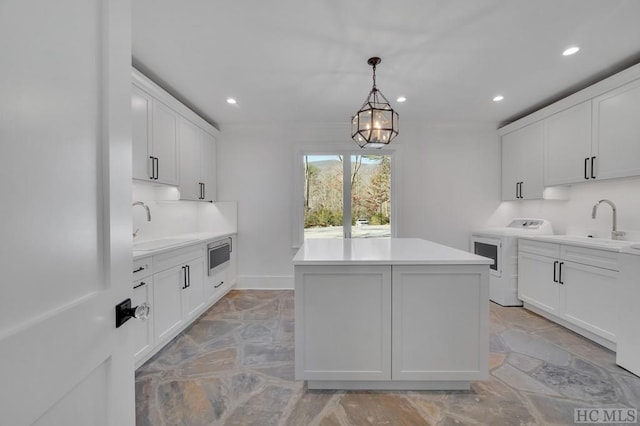 kitchen with washer / clothes dryer, sink, a kitchen island, and white cabinets