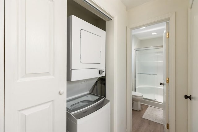 clothes washing area with stacked washer / dryer, laundry area, and wood finished floors