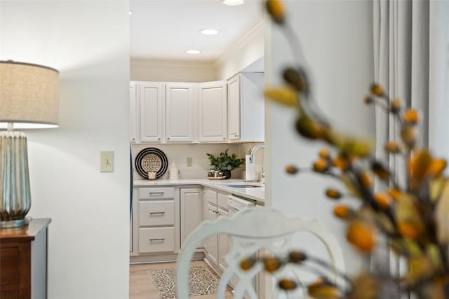 interior space with a sink, ornamental molding, recessed lighting, light countertops, and white cabinets