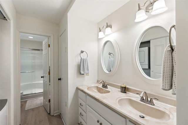full bathroom with a sink, a shower with shower door, double vanity, and wood finished floors