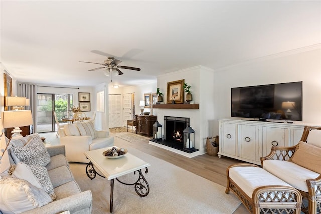 living room featuring crown molding, a lit fireplace, wood finished floors, and ceiling fan