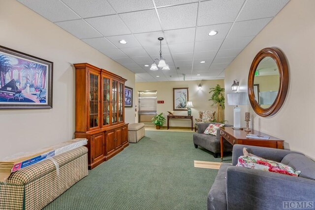 living area featuring a drop ceiling, a notable chandelier, and carpet flooring