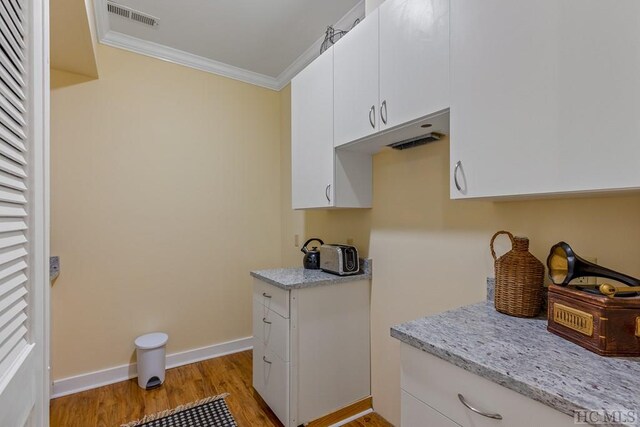 kitchen featuring white cabinetry, crown molding, light stone countertops, and light wood-type flooring