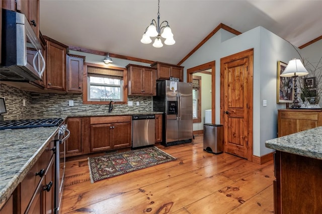 kitchen with decorative light fixtures, vaulted ceiling, stainless steel appliances, stone counters, and backsplash