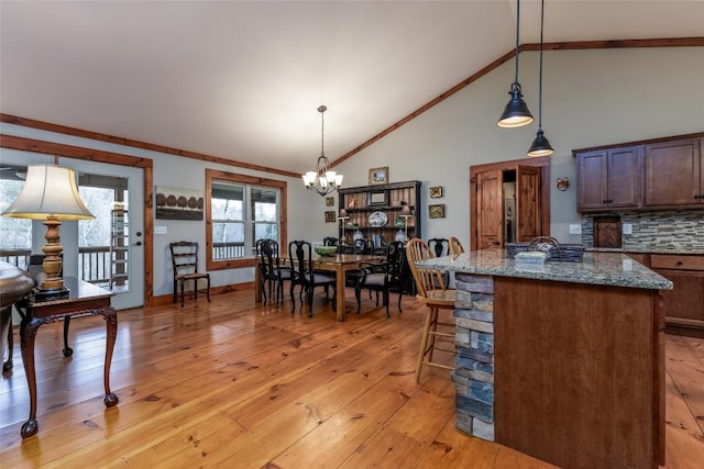 kitchen featuring tasteful backsplash, hanging light fixtures, light wood-style flooring, stone countertops, and a chandelier