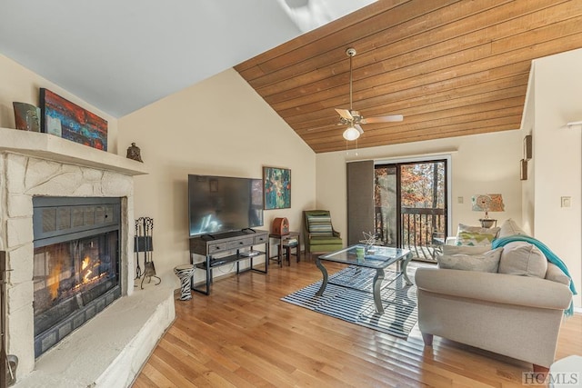 living room with vaulted ceiling, a stone fireplace, ceiling fan, wood ceiling, and light wood-type flooring