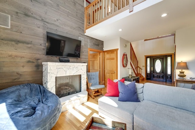 living area featuring stairway, a high ceiling, wood walls, recessed lighting, and a fireplace