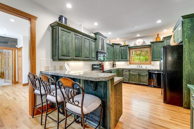 kitchen with green cabinetry, black appliances, a sink, a peninsula, and recessed lighting