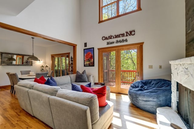 living room with a towering ceiling, wood finished floors, healthy amount of natural light, and a stone fireplace
