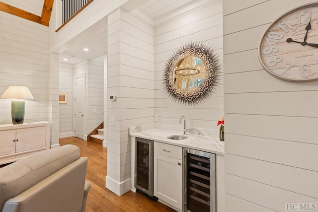 bar featuring wooden walls, beverage cooler, sink, and light wood-type flooring