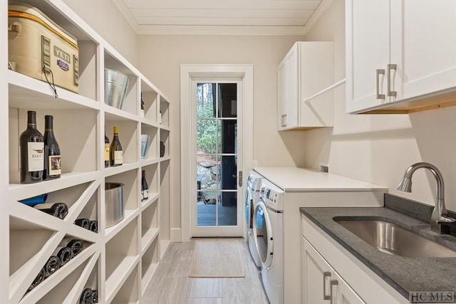 clothes washing area featuring sink, washer and clothes dryer, cabinets, ornamental molding, and light wood-type flooring