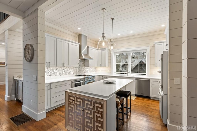 kitchen featuring wall chimney range hood, appliances with stainless steel finishes, dark hardwood / wood-style floors, a center island, and decorative backsplash