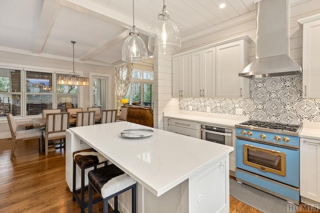 kitchen with wall chimney exhaust hood, white cabinetry, hanging light fixtures, a kitchen island, and stove