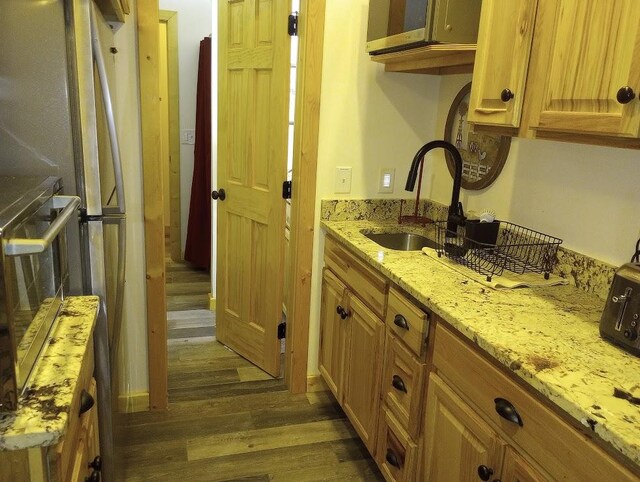 kitchen with light stone counters, sink, wall oven, and dark hardwood / wood-style floors