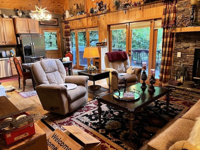 living room with a stone fireplace, a notable chandelier, high vaulted ceiling, and light hardwood / wood-style flooring