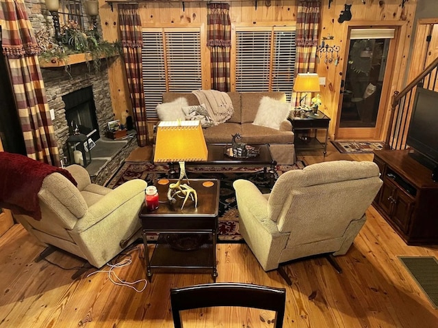 living room featuring a stone fireplace, wooden walls, and light hardwood / wood-style floors