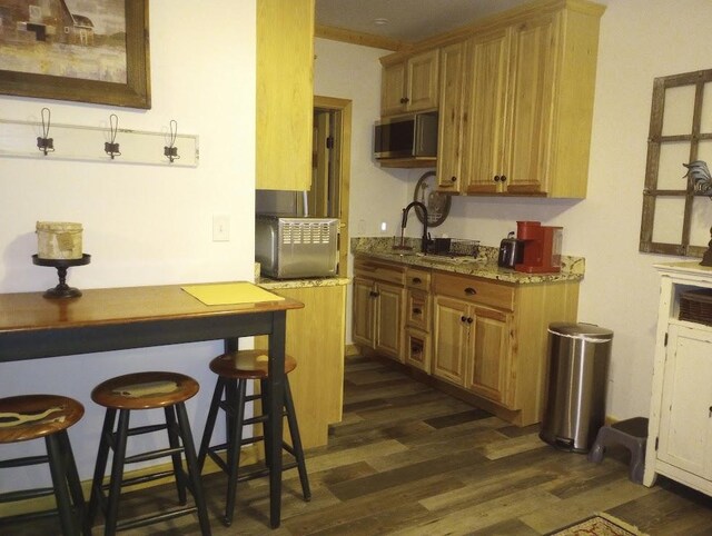 kitchen with sink, a breakfast bar area, light stone countertops, and dark hardwood / wood-style floors