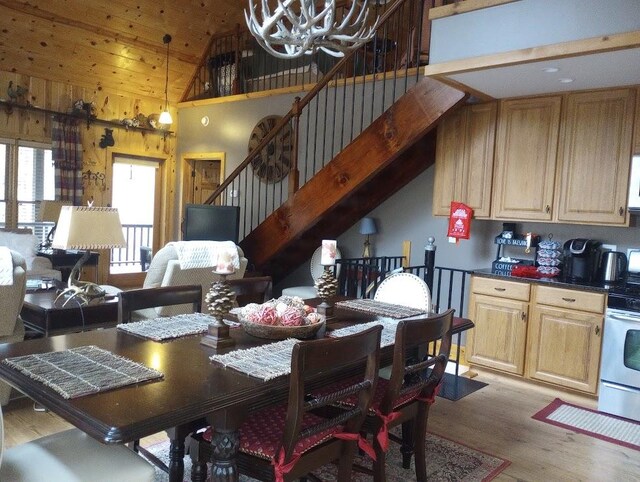 dining area with light hardwood / wood-style flooring, high vaulted ceiling, wooden walls, and a chandelier