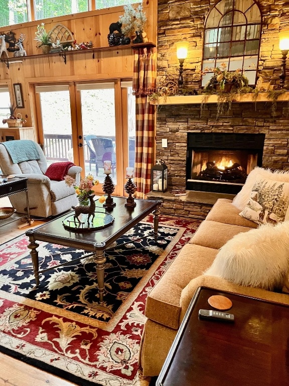 living room with hardwood / wood-style floors, a stone fireplace, wood walls, and a towering ceiling