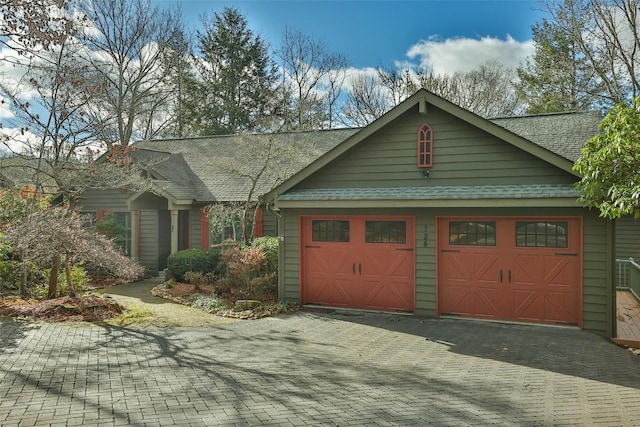 view of front facade with decorative driveway, a garage, and roof with shingles