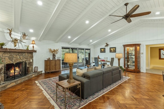 living room with lofted ceiling with beams, wooden walls, a stone fireplace, and ceiling fan