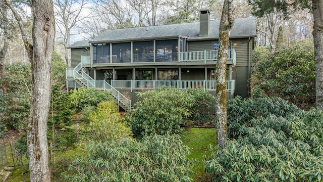 back of property with a chimney, a shingled roof, stairs, and a sunroom