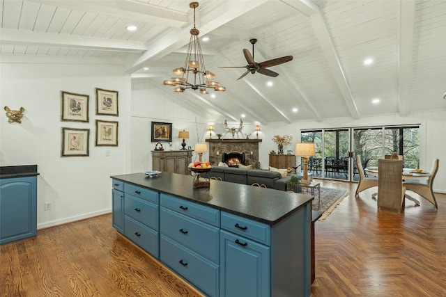 kitchen featuring dark countertops, a center island, beamed ceiling, a stone fireplace, and blue cabinets