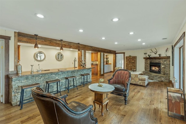 living area featuring ornamental molding, wood finished floors, recessed lighting, a stone fireplace, and wet bar