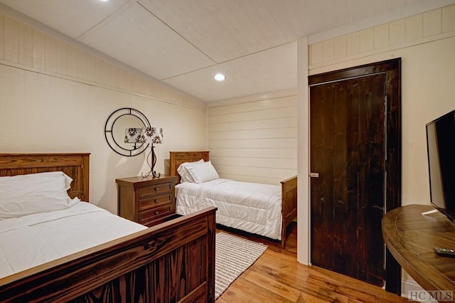 bedroom with vaulted ceiling, light hardwood / wood-style floors, and wood walls