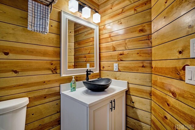 bathroom with vanity, toilet, and wood walls