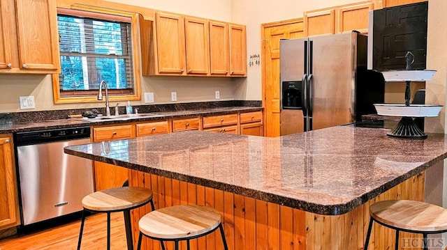 kitchen with appliances with stainless steel finishes, light wood-type flooring, dark stone counters, sink, and a kitchen bar