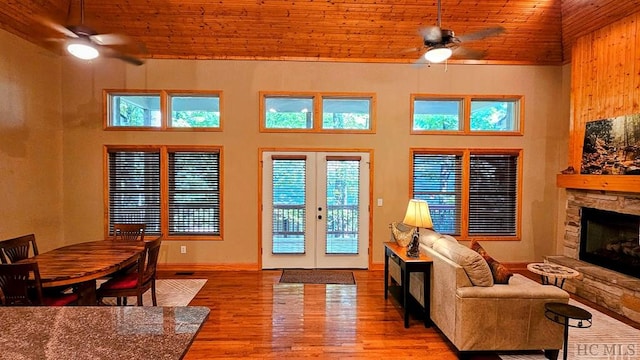 doorway with a stone fireplace, french doors, high vaulted ceiling, wooden ceiling, and light wood-type flooring