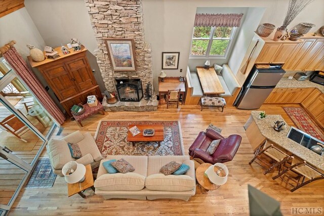 sitting room featuring light hardwood / wood-style flooring, a high ceiling, and a stone fireplace