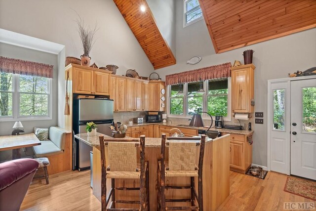 kitchen featuring light brown cabinets, a kitchen breakfast bar, backsplash, stainless steel fridge, and high vaulted ceiling