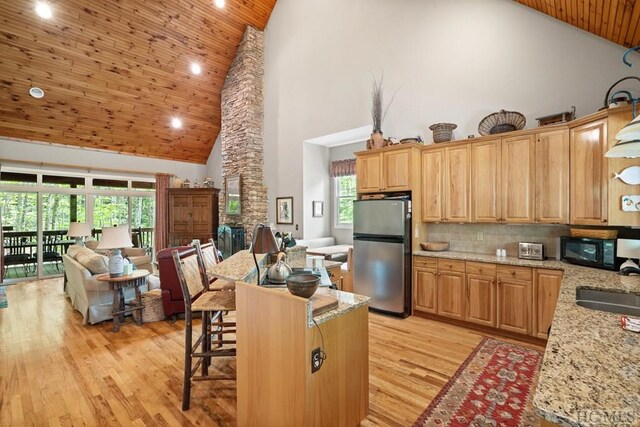 kitchen featuring decorative backsplash, high vaulted ceiling, light stone countertops, and stainless steel refrigerator